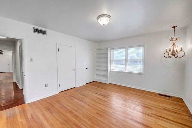1600 W Kansas Ave, Midland, TX 79701 - unfurnished bedroom with light wood finished floors, a chandelier, and two closets