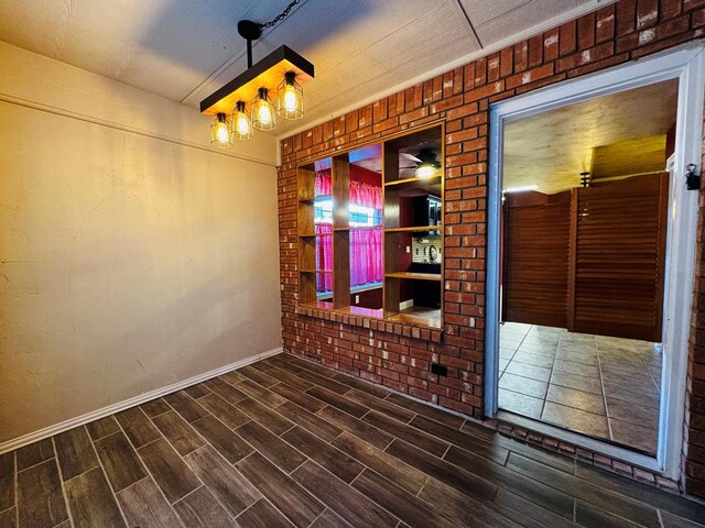 8801 N Rice Ave, Odessa, TX 79765 - spare room featuring dark wood-style flooring, baseboards, and brick wall