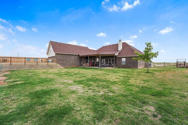 back of property featuring brick siding, a fenced backyard, a chimney, a patio area, and a lawn