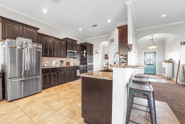 kitchen featuring dark brown cabinetry, a breakfast bar area, appliances with stainless steel finishes, arched walkways, and a sink