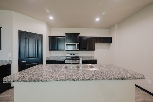 kitchen with light stone countertops, recessed lighting, a sink, stainless steel appliances, and an island with sink