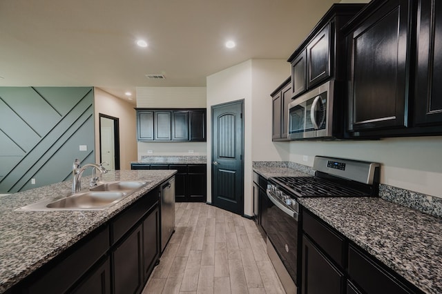 kitchen featuring light wood-style flooring, dark cabinetry, visible vents, a sink, and appliances with stainless steel finishes
