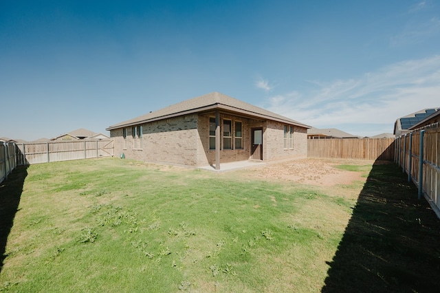 rear view of property featuring a yard, brick siding, and a fenced backyard
