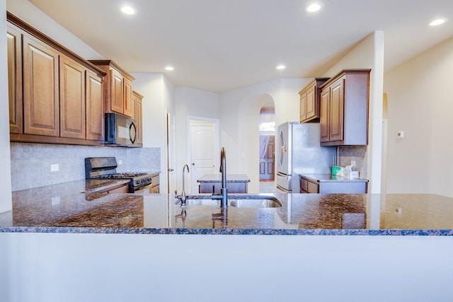 kitchen with black microwave, arched walkways, a sink, stainless steel gas range, and freestanding refrigerator