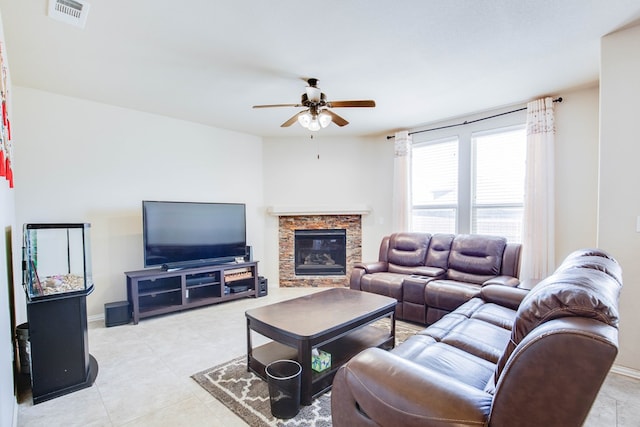 living area with visible vents, light tile patterned flooring, baseboards, a stone fireplace, and ceiling fan