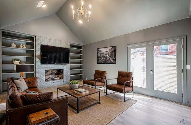 living room featuring a brick fireplace, a chandelier, light wood-type flooring, vaulted ceiling, and french doors