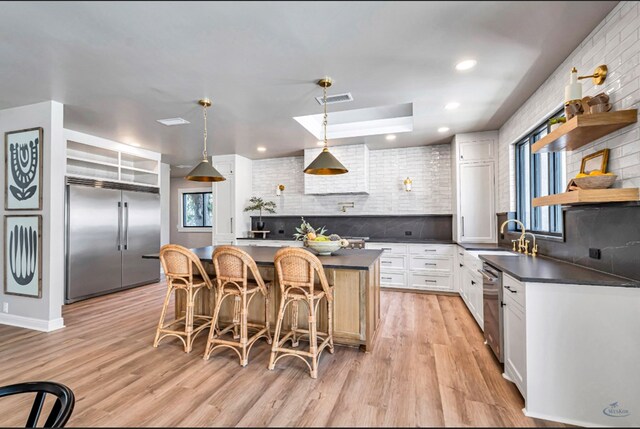 kitchen featuring a kitchen island, open shelves, a sink, built in refrigerator, and dark countertops