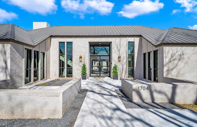 property entrance featuring stucco siding, a chimney, and french doors