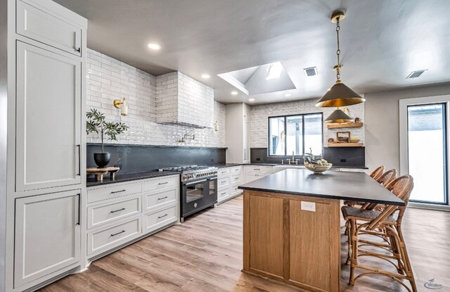 kitchen featuring dark countertops, visible vents, light wood-type flooring, a skylight, and high end range