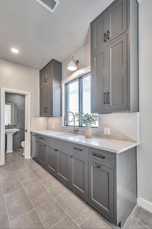 kitchen with tasteful backsplash, gray cabinetry, visible vents, and a sink