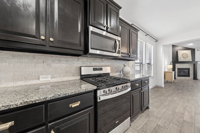 7410 W Pile Ranch Rd, Odessa, TX 79765 - kitchen with stainless steel appliances, decorative backsplash, light stone countertops, and a glass covered fireplace