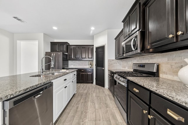 7410 W Pile Ranch Rd, Odessa, TX 79765 - kitchen featuring stainless steel appliances, light wood finished floors, light stone counters, white cabinets, and decorative backsplash