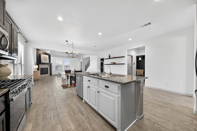 7410 W Pile Ranch Rd, Odessa, TX 79765 - kitchen featuring stainless steel appliances, light wood finished floors, dark stone counters, a center island with sink, and a chandelier