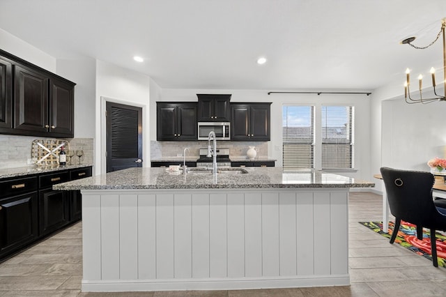 7410 W Pile Ranch Rd, Odessa, TX 79765 - kitchen with stainless steel microwave, dark cabinetry, tasteful backsplash, a kitchen island with sink, and recessed lighting