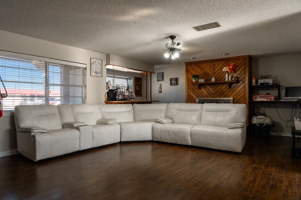 living room featuring visible vents, wood finished floors, baseboards, ceiling fan, and a textured ceiling