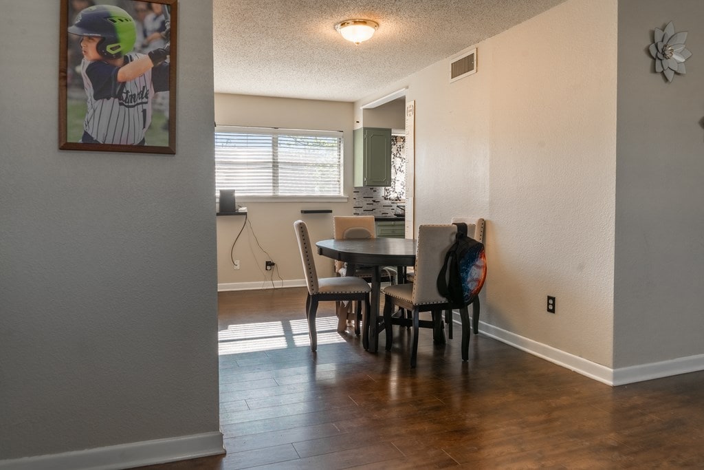 dining room with baseboards, a textured ceiling, wood finished floors, and visible vents