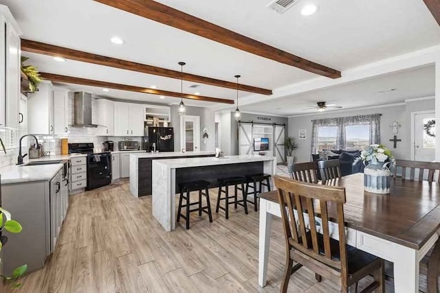 dining area featuring sink, ceiling fan, a barn door, light wood-type flooring, and beamed ceiling