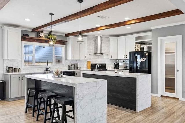 kitchen featuring black appliances, white cabinets, a center island with sink, wall chimney exhaust hood, and a breakfast bar area