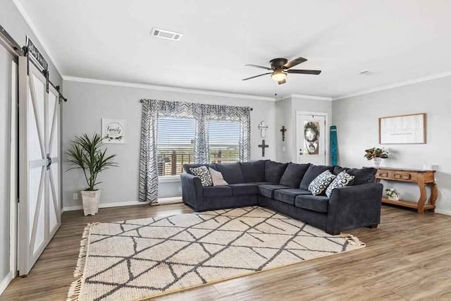 living room featuring a barn door, ceiling fan, hardwood / wood-style floors, and ornamental molding