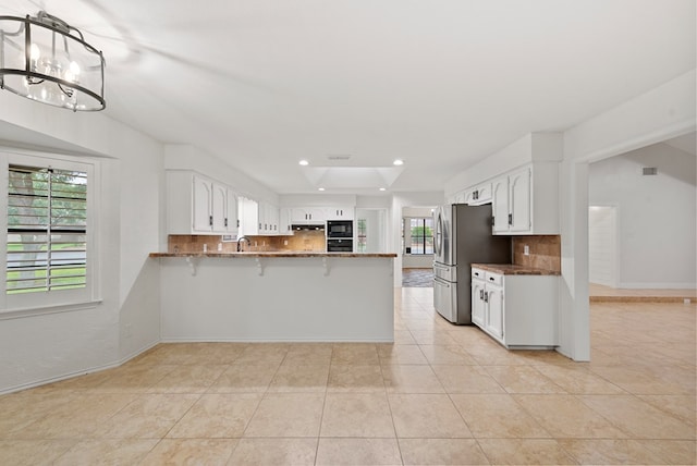 20 Sunnygrove Dr, Odessa, TX 79761 - kitchen featuring a peninsula, decorative backsplash, dark stone countertops, light tile patterned floors, and freestanding refrigerator