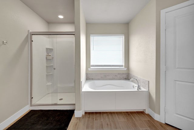 bathroom with a bath, a stall shower, wood finished floors, and baseboards