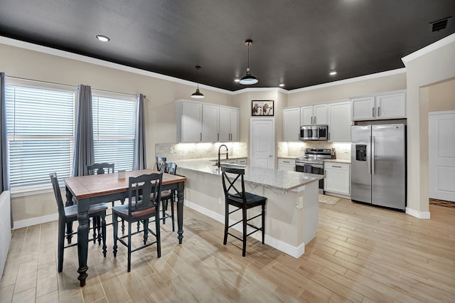 kitchen with stainless steel appliances, a peninsula, backsplash, crown molding, and white cabinetry