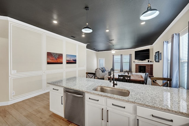 kitchen with dishwasher, a sink, a fireplace, hanging light fixtures, and white cabinetry