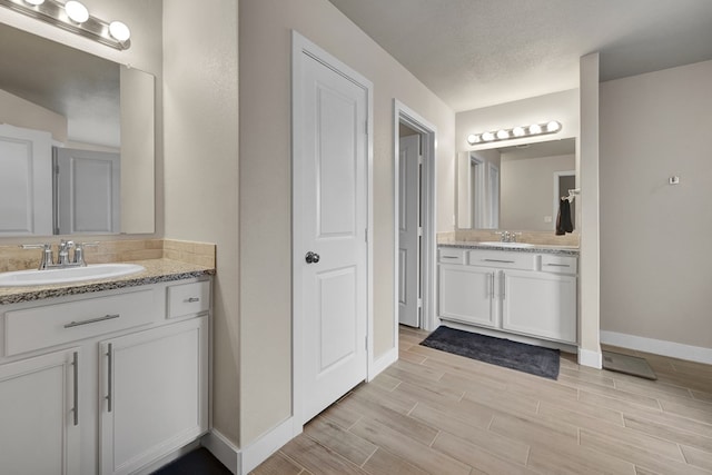 full bathroom featuring baseboards, two vanities, and wood finished floors
