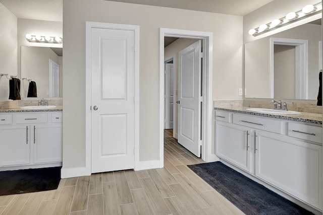 full bath featuring wood finish floors, two vanities, and baseboards