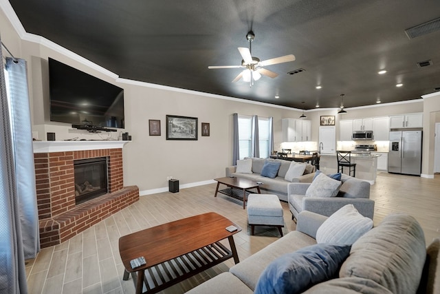 living room featuring ceiling fan, a fireplace, baseboards, light wood-type flooring, and crown molding