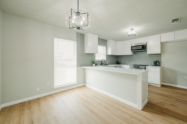 1613 E 52nd St, Odessa, TX 79762 - kitchen with stainless steel appliances, light wood-type flooring, light countertops, a chandelier, and white cabinets