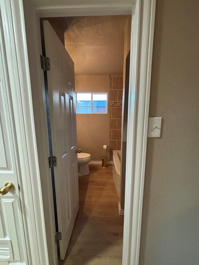 314 SW 11th Pl, Andrews, TX 79714 - full bath featuring toilet, wood finished floors, a bathtub, a textured ceiling, and a textured wall