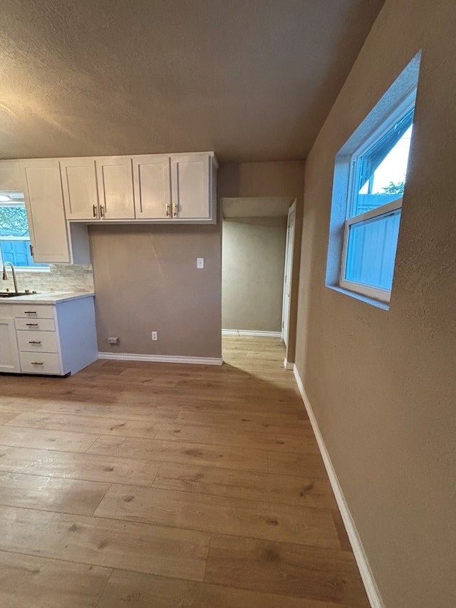 314 SW 11th Pl, Andrews, TX 79714 - kitchen featuring a sink, white cabinets, light wood finished floors, backsplash, and a textured ceiling