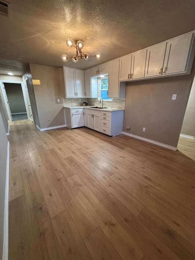314 SW 11th Pl, Andrews, TX 79714 - kitchen featuring white cabinetry, baseboards, a sink, light countertops, and light wood-style flooring