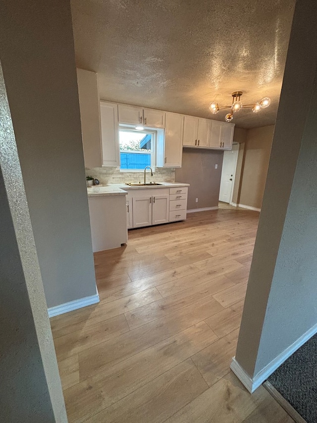 314 SW 11th Pl, Andrews, TX 79714 - kitchen with a sink, white cabinets, baseboards, light wood-style floors, and a textured ceiling