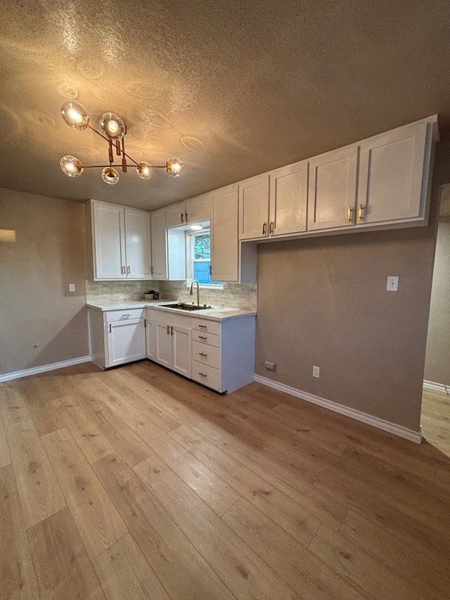 314 SW 11th Pl, Andrews, TX 79714 - kitchen featuring a sink, white cabinetry, light wood-style flooring, light countertops, and decorative backsplash