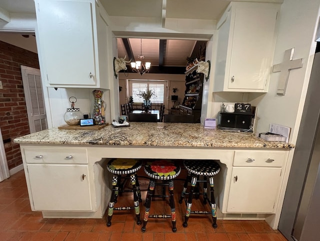 kitchen featuring a breakfast bar, beamed ceiling, light stone countertops, white cabinets, and a chandelier