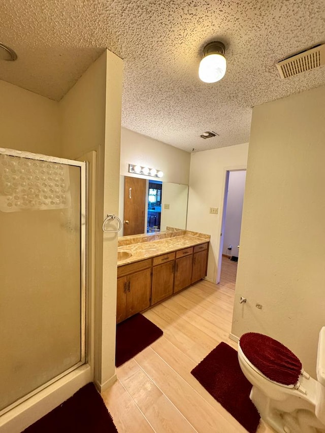 bathroom featuring a textured ceiling, wood finished floors, visible vents, a shower stall, and double vanity