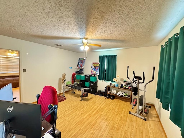 exercise area featuring visible vents, a textured ceiling, wood finished floors, and a ceiling fan