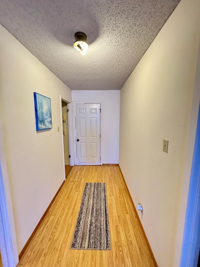 hallway featuring a textured ceiling, baseboards, and light wood-style floors