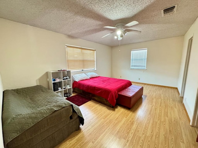 bedroom featuring baseboards, visible vents, a ceiling fan, wood finished floors, and a textured ceiling