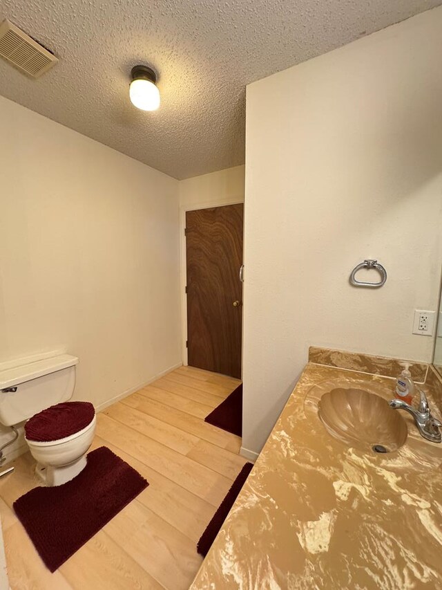 half bathroom featuring visible vents, toilet, vanity, a textured ceiling, and wood finished floors