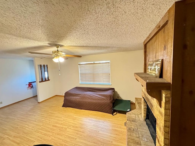 bedroom featuring a textured ceiling, light wood-style flooring, a fireplace, a ceiling fan, and baseboards