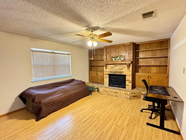 bedroom with a textured ceiling, a brick fireplace, wood finished floors, and visible vents