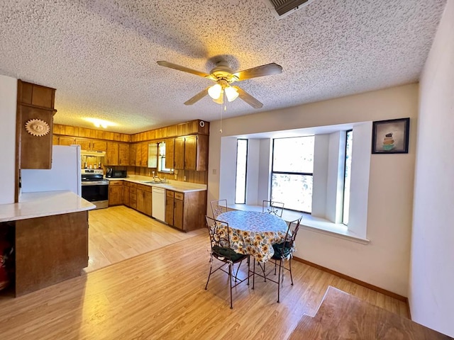 kitchen with brown cabinetry, light wood-type flooring, white appliances, and light countertops