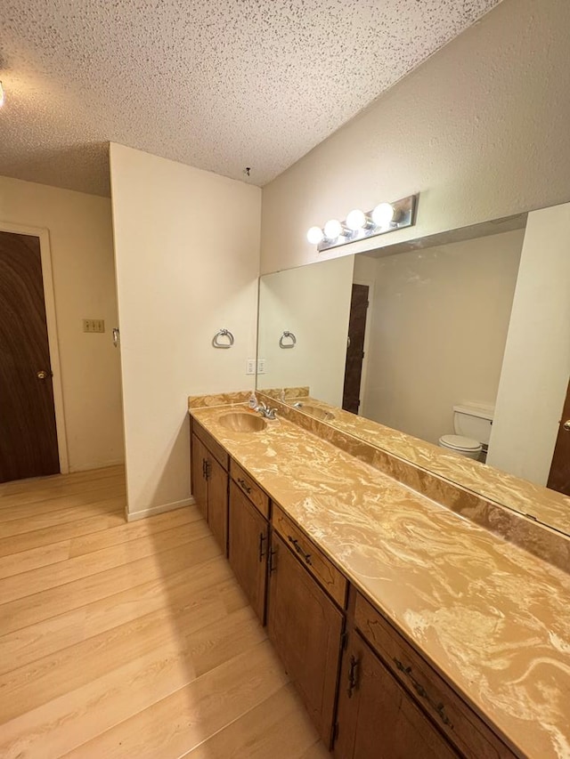 full bathroom with a textured ceiling, toilet, wood finished floors, a sink, and double vanity