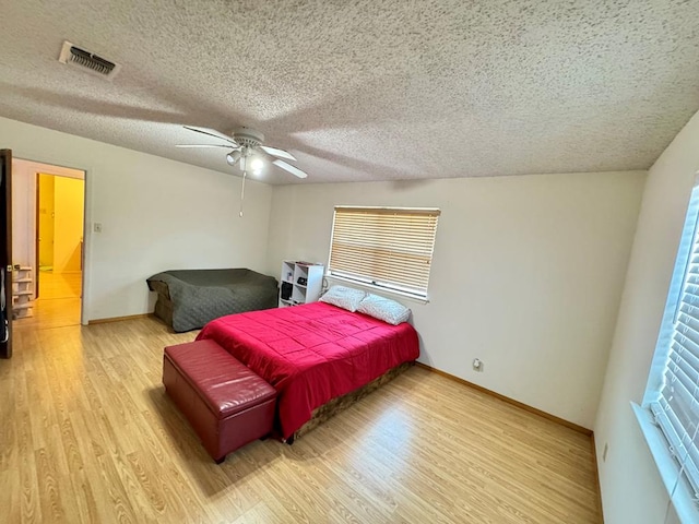 bedroom with visible vents, a textured ceiling, baseboards, and wood finished floors