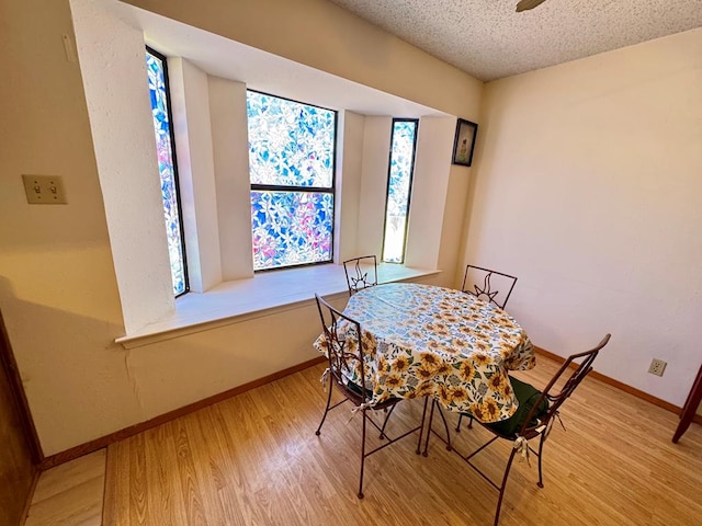 dining room featuring baseboards, a textured ceiling, and light wood finished floors