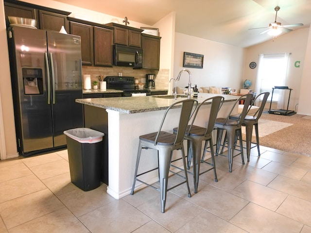 kitchen featuring decorative backsplash, a kitchen island with sink, a kitchen bar, a sink, and black appliances