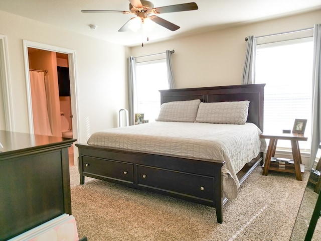 bedroom with a ceiling fan, ensuite bath, and light colored carpet